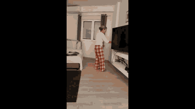 a woman in plaid pants is standing in front of a television