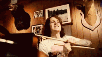 a man is holding a bow and arrow in a room with a deer head on the wall behind him