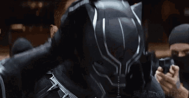 a man wearing a black panther helmet is surrounded by men in black masks