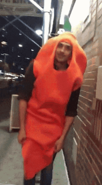 a man in an orange carrot costume stands in front of a brick building
