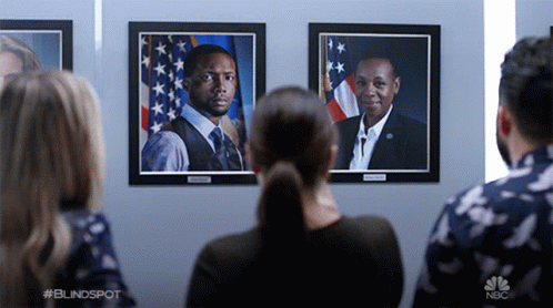 a group of people are looking at portraits of a man and a woman on a wall with nbc written on the bottom