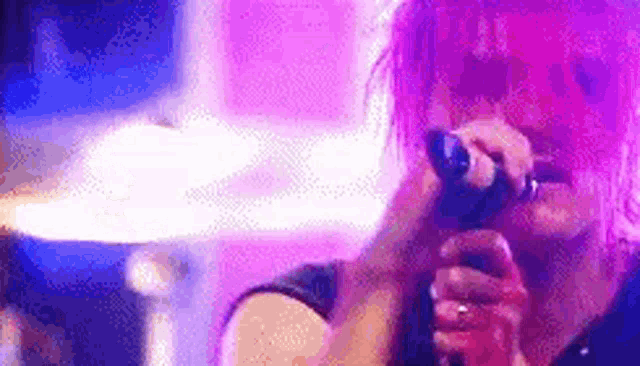 a woman with pink hair is singing into a microphone in front of a purple background .