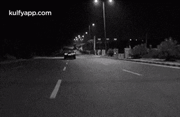 a black and white photo of a car driving down a city street at night .