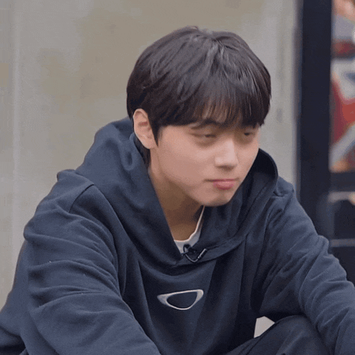 a young man wearing a black hoodie with the letter d on the front sits down
