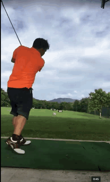 a man in an orange shirt swings a golf club