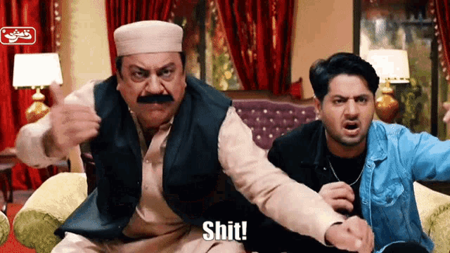 two men are sitting on a couch and one is saying shit