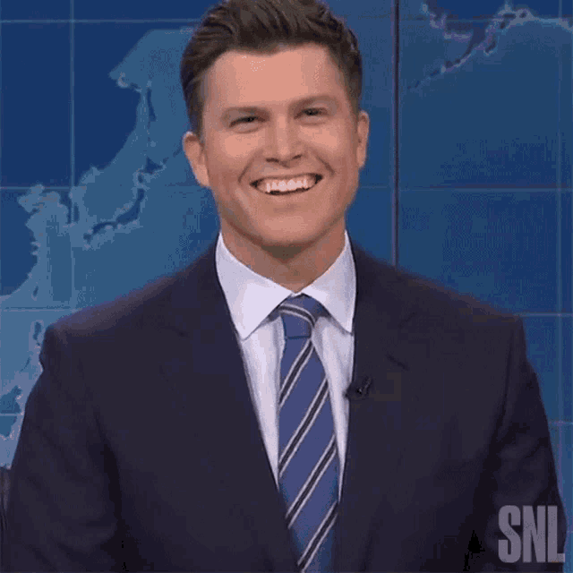 a man in a suit and tie is smiling with the snl logo in the background