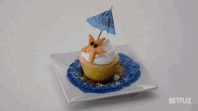 a cupcake with a starfish and an umbrella on top of it on a white plate with netflix written on the bottom