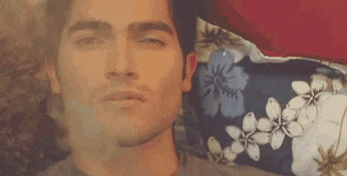 a man is laying on a bed with his eyes closed and a floral pillow .