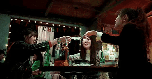 a group of women are sitting at a table with bottles of alcohol and toasting .