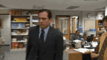 a man in a suit and tie walks through an office with a clock on the wall