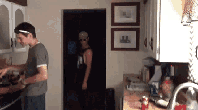 a man in a black tank top with the letter a on it stands in the kitchen