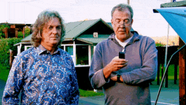 two men are standing next to each other one is looking at his phone