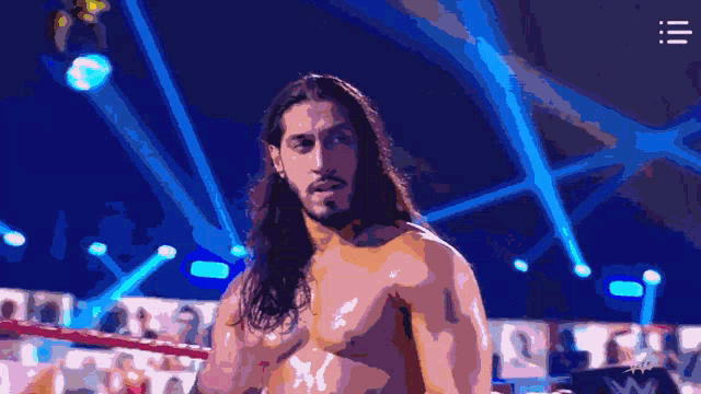 a shirtless wrestler with long hair stands in a ring