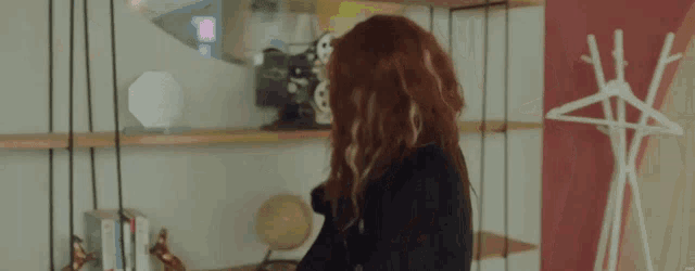 a woman with red hair is standing in front of a shelf with a globe on it .