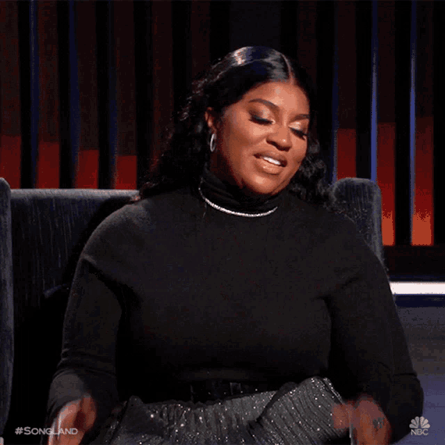 a woman wearing a black turtleneck is sitting in a chair with her hands in the air and the words songland on the bottom
