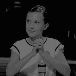 a black and white photo of a woman sitting at a table with her hands folded in prayer