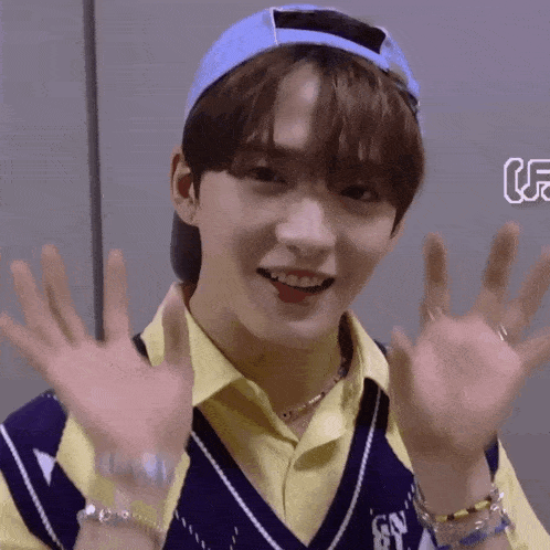 a young boy wearing a blue hat and a yellow shirt is waving his hands .