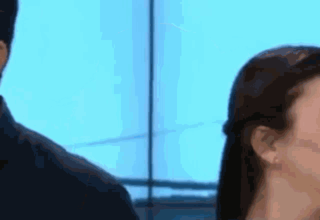 a man and a woman are standing next to each other in front of a window . the woman is wearing earrings .