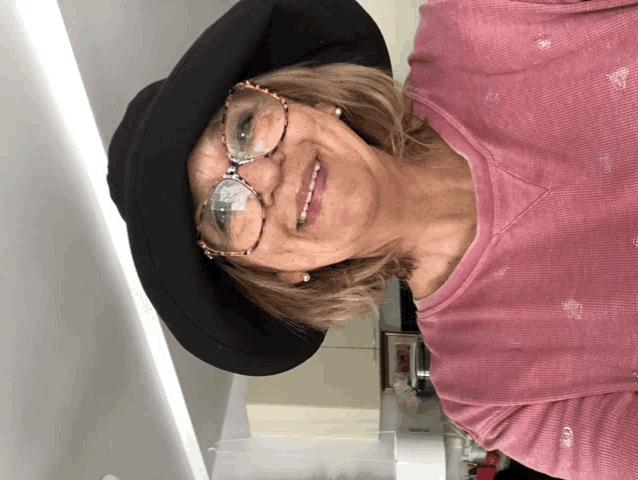 a woman wearing glasses and a hat is smiling for the camera