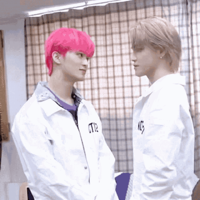 two men are standing next to each other in a room and looking at each other . one of the men has pink hair .