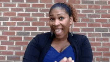 a woman is smiling in front of a brick wall while wearing a blue shirt .