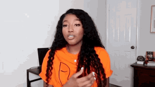a woman with long curly hair is wearing an orange t-shirt with a face on it .