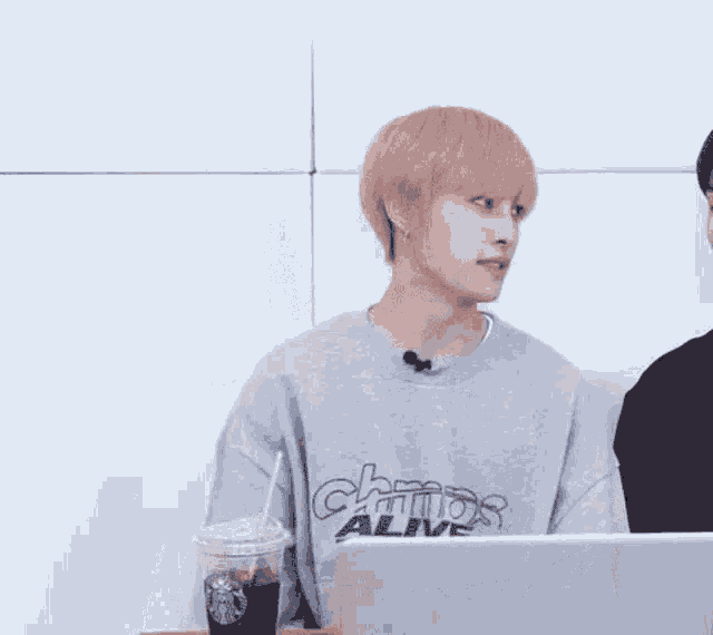a man wearing a sweatshirt with the word alive on it is sitting in front of a laptop .