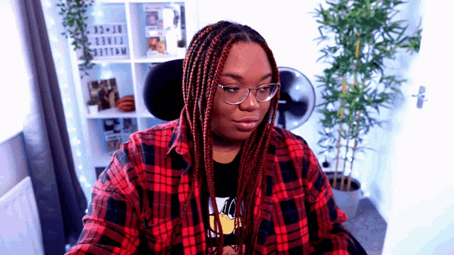 a woman wearing glasses and a plaid shirt is sitting in front of a plant