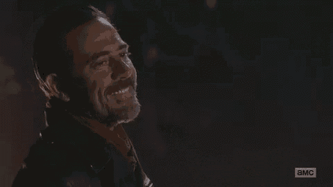 a man with a beard is smiling in the dark while wearing a leather jacket and scarf .