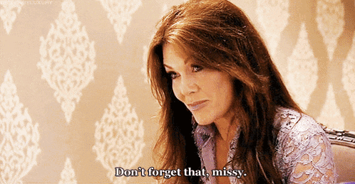 a woman is sitting in front of a wall with a pattern and says " don 't forget that missy "