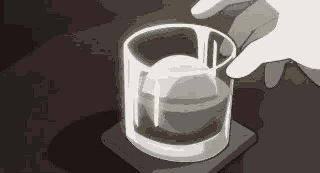 a hand is reaching for a glass of whiskey with an ice ball in it
