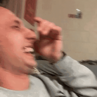 a man is sitting on a couch laughing while holding a piece of paper in his mouth .