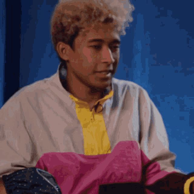 a man with curly hair wearing a pink and yellow shirt