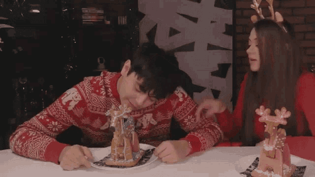 a man wearing a red sweater with elephants on it is eating a gingerbread house