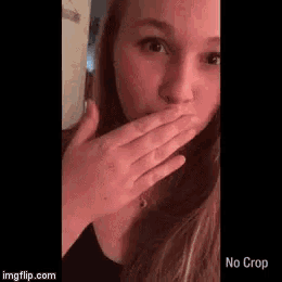 a woman is covering her mouth with her hand and looking at the camera .