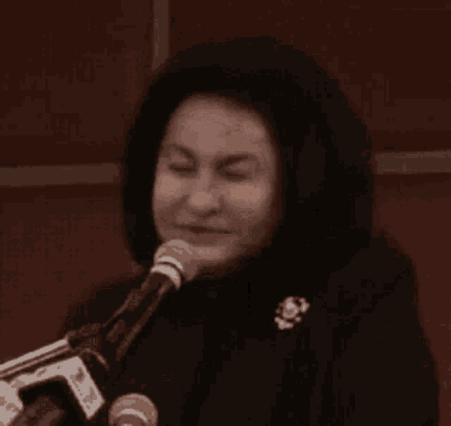 a woman is speaking into a microphone while wearing a black coat .