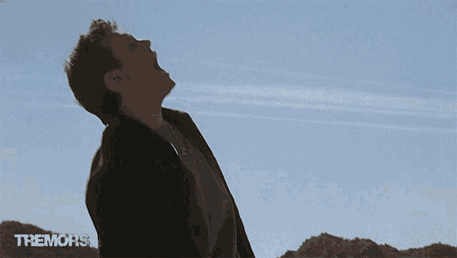 a man is screaming in front of a blue sky with the word tremors on the bottom