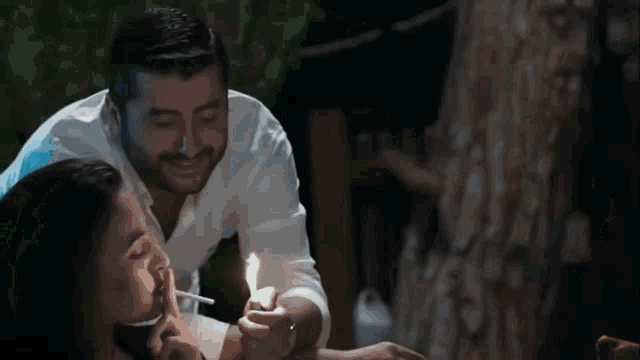 a man is lighting a cigarette for a woman while they are sitting at a table .