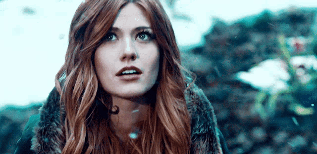 a woman with long red hair and a fur coat is looking up .
