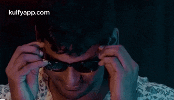 a man is wearing sunglasses in a dark room and looking down .