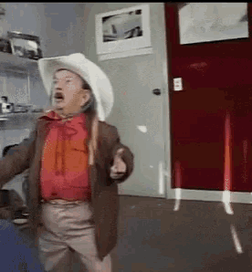 a man in a cowboy hat is pointing at something in a room