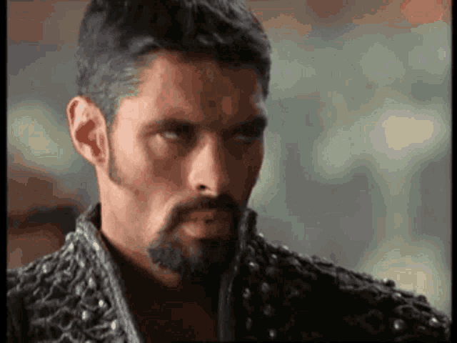 a man with a beard is wearing a black jacket with studs .