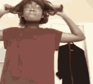a person wearing glasses and a red shirt is holding their hair in their hands .