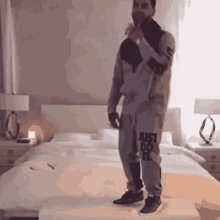 a man is standing on a stool in front of a bed holding a microphone .