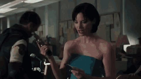 a woman in a strapless blue dress is holding a gun in her hand .