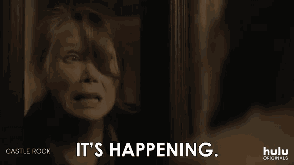 a woman is standing in front of a door with the words `` it 's happening '' written on the screen .