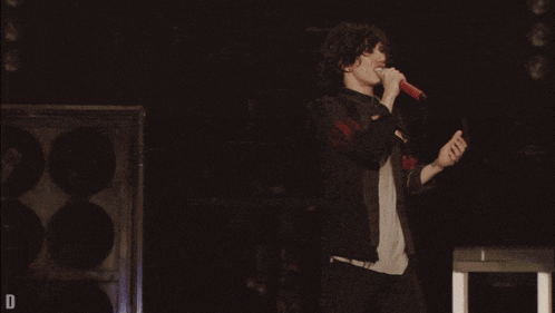 a man singing into a microphone on a stage with the letter d below him