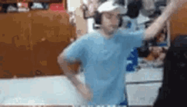 a man in a blue shirt and white hat is standing in a room with his arms outstretched .