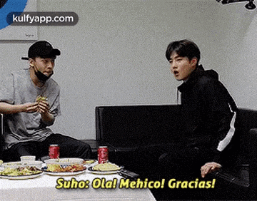 two men are sitting at a table with plates of food and drinks and talking .